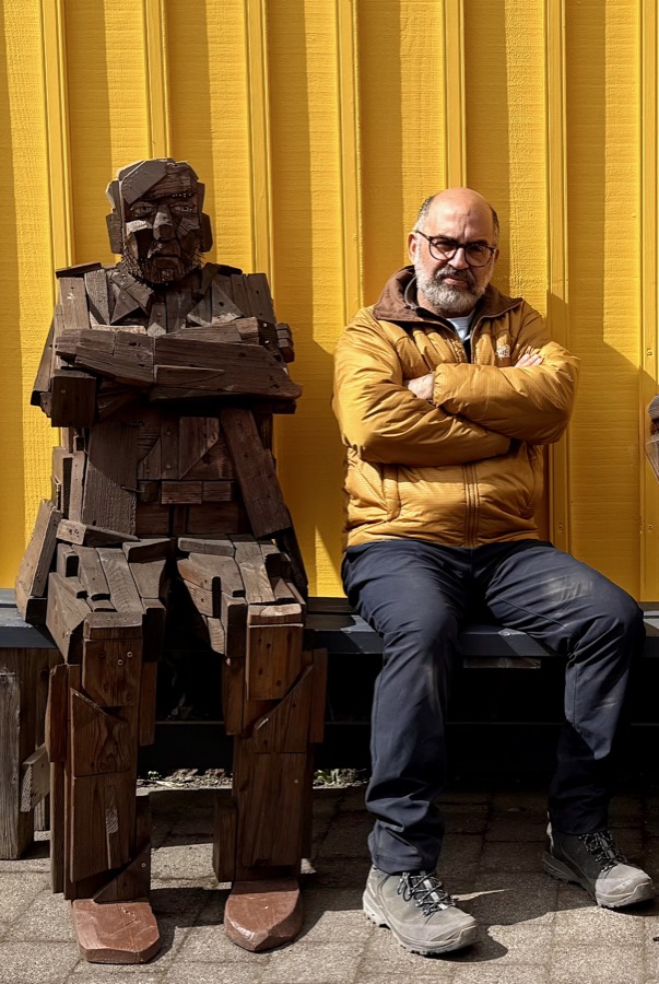 Robert Sfeir, founder and CEO of Kyroco, sitting on a bench next to a life-size wooden sculpture of a seated man